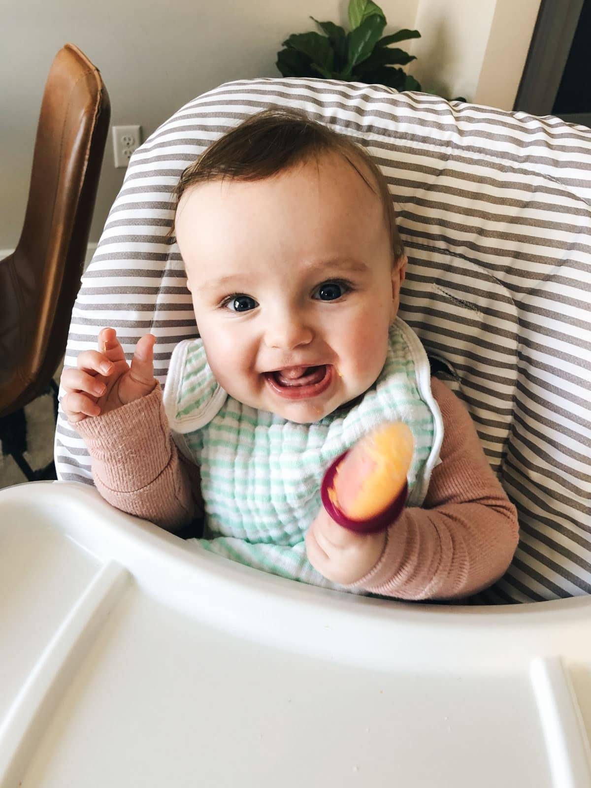 Solvi in a high chair smiling at the camera.