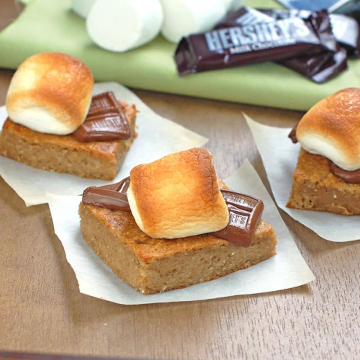 Graham bars topped with melted chocolate and fluffy marshmallows on parchment paper.