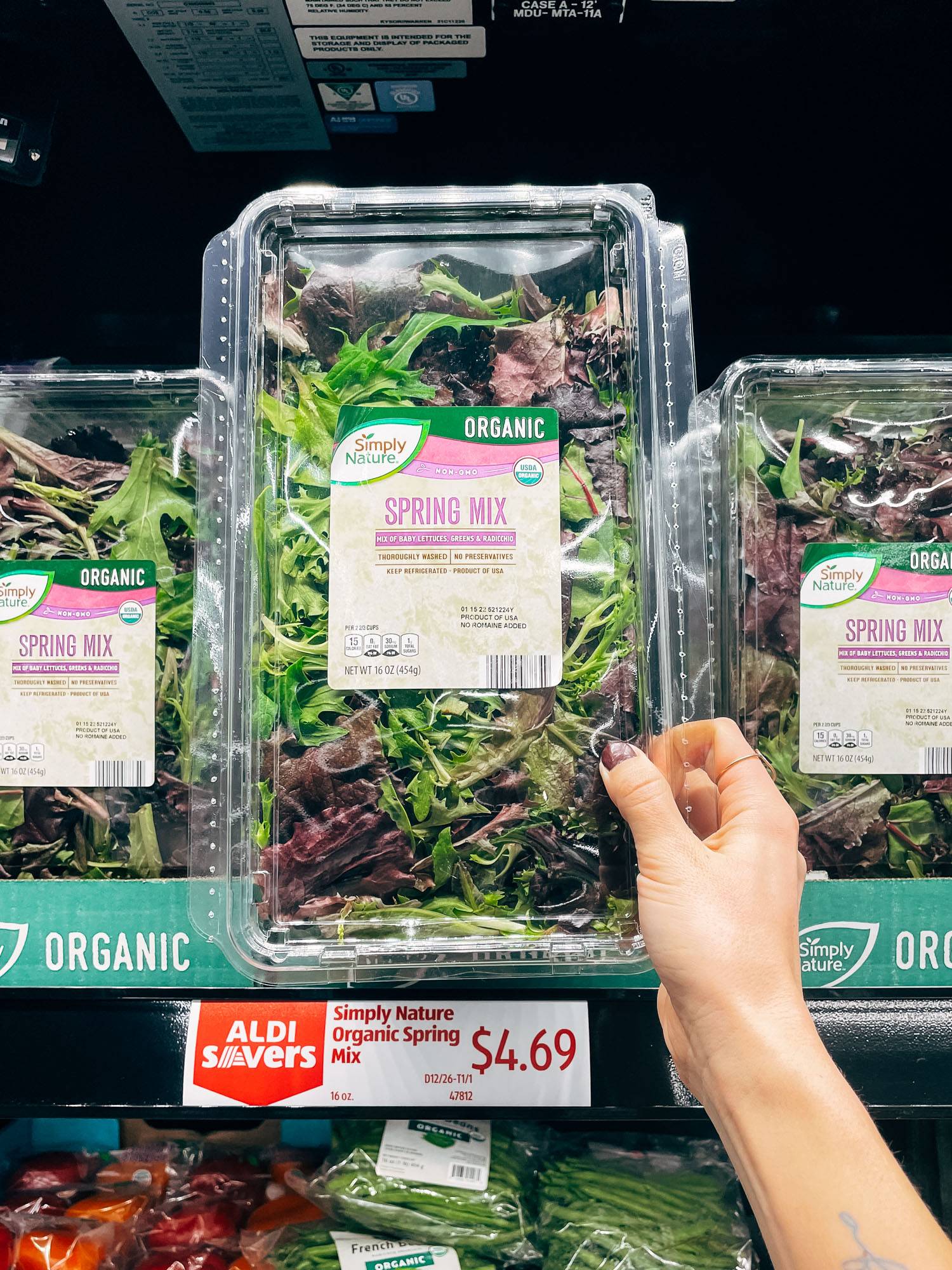 White hand holding package of spring mix.