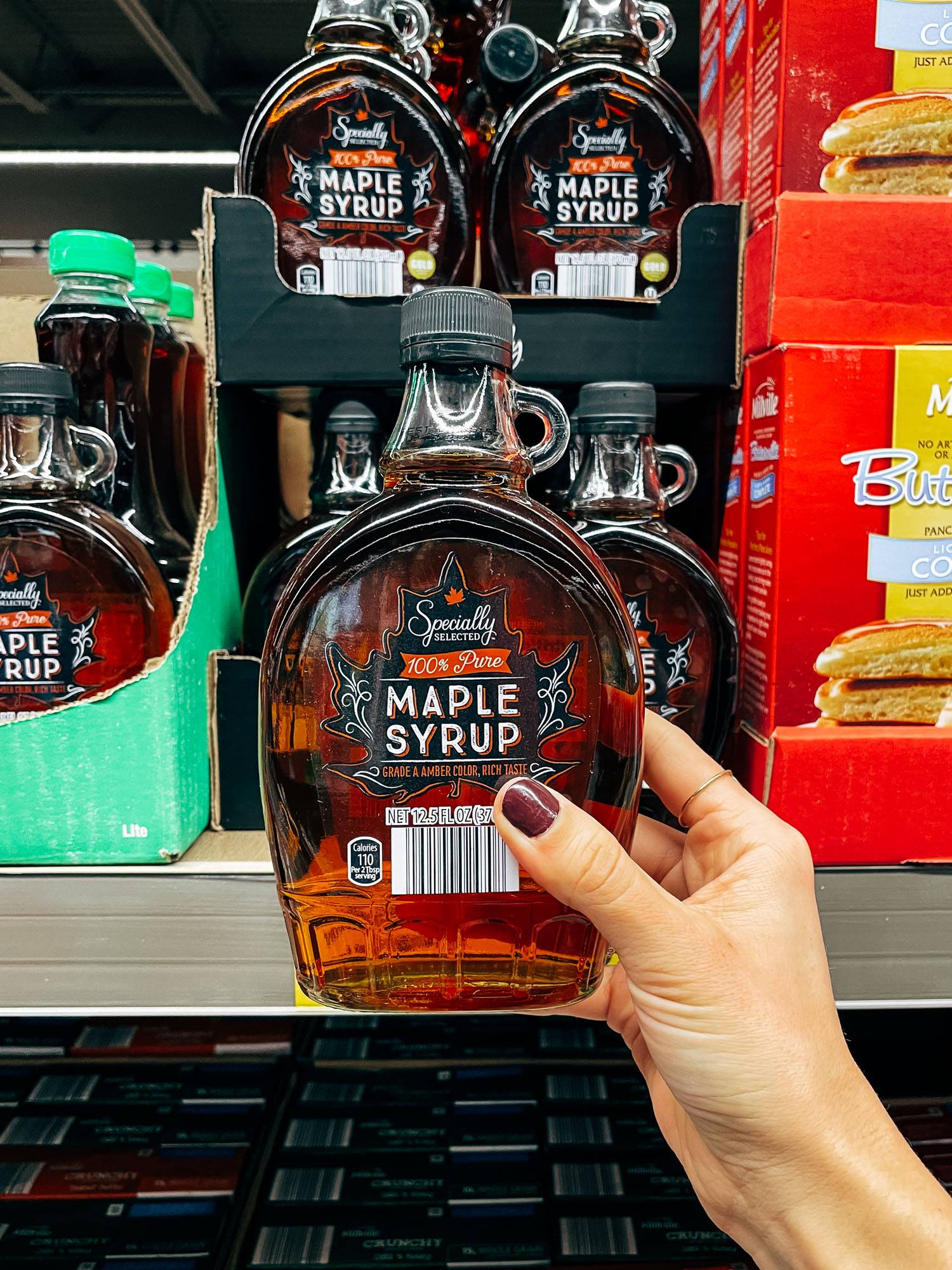 White hand holding a container of maple syrup