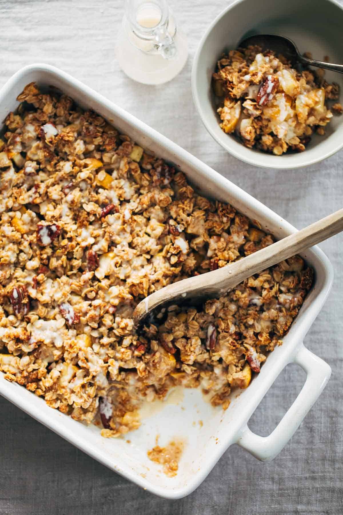 Coconut Oil Apple Crisp in a white baking dish with a wooden spoon.
