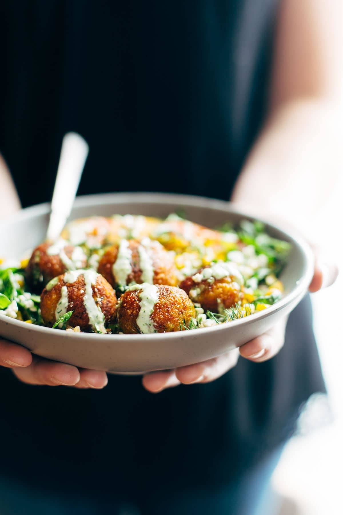 Hands holding Summer Bliss Bowls with Sweet Potato Falafel and Jalapeño Ranch.
