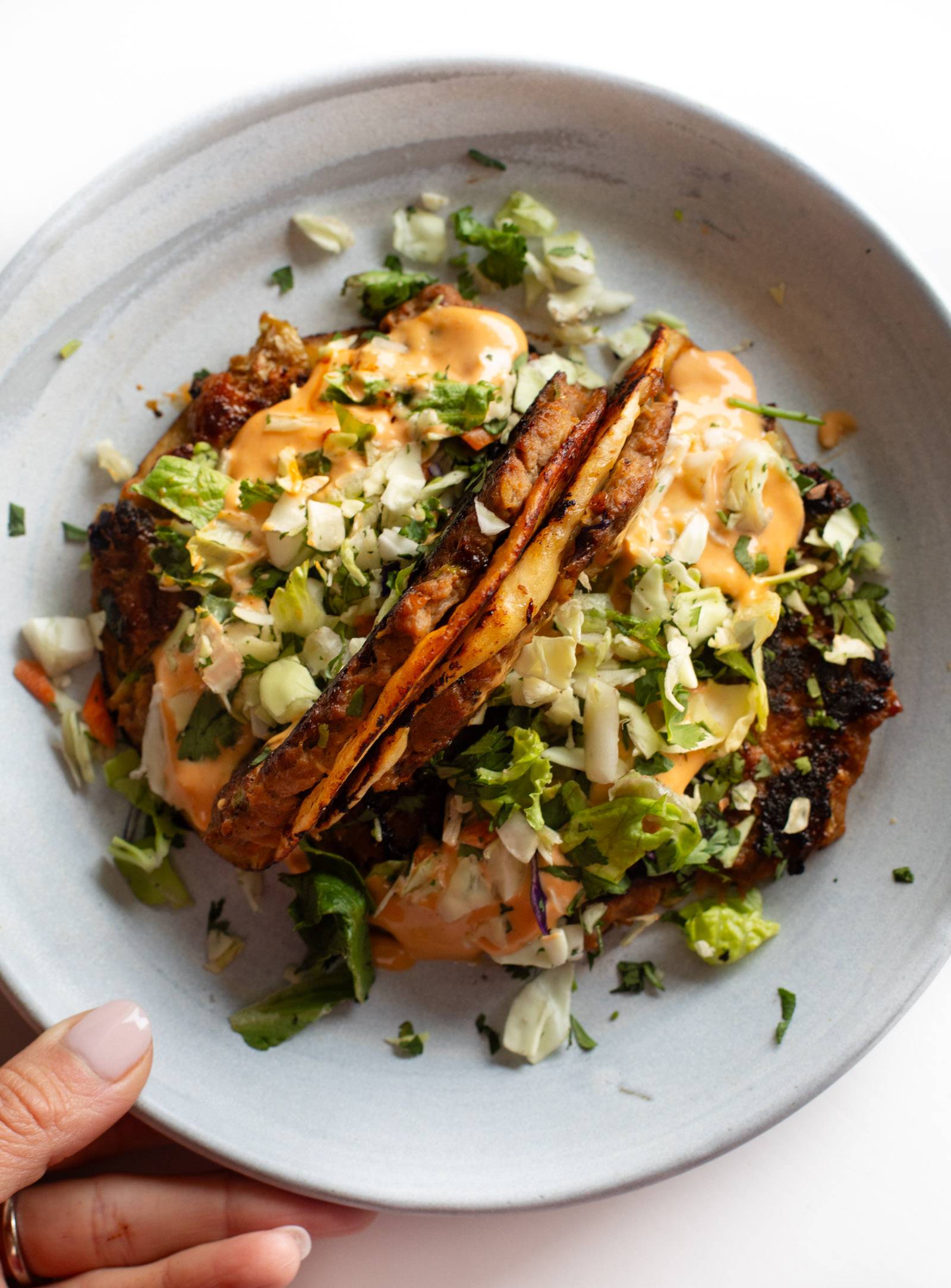 Two egg roll tacos on a plate topped with gochujang sauce.