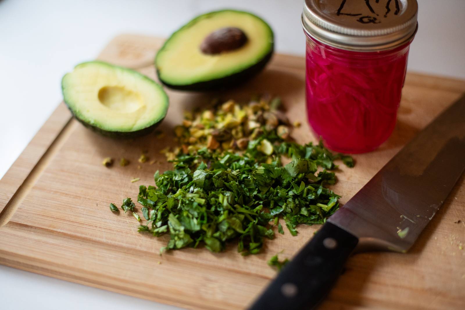 Chopped herbs, pistachios, and avocado with jar of pickled onions.